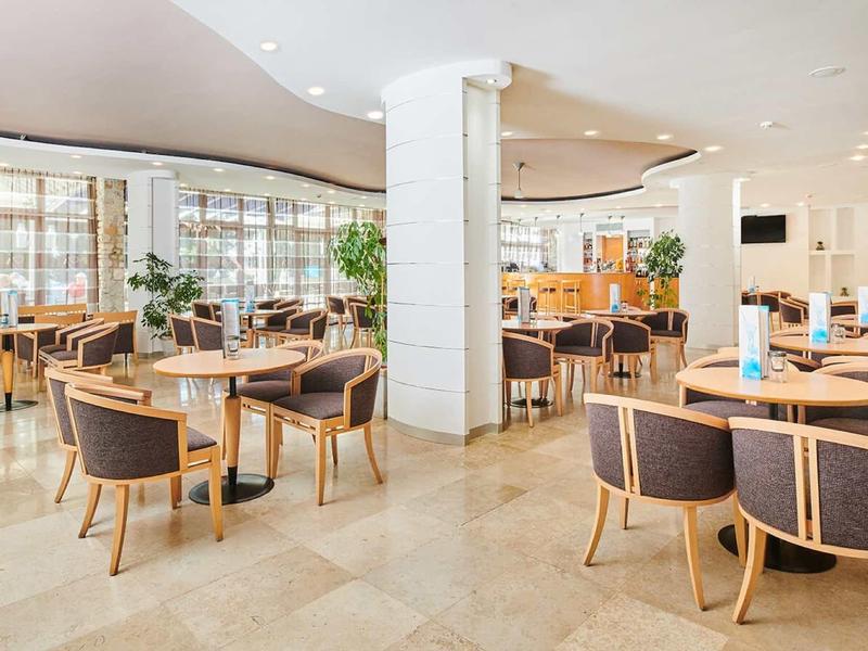 Heller, großer Gastraum mit braunen Stühlen, mehreren Tischen und großen Fenstern mit Gardinen.