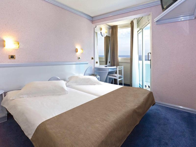 Kleines Hotelzimmer mit Doppelbett, hellen Wänden und Balkon mit Aussicht.