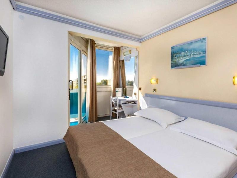 Kleines Hotelzimmer mit Doppelbett, Fernseher, Schreibtisch und Balkon mit Meerblick.