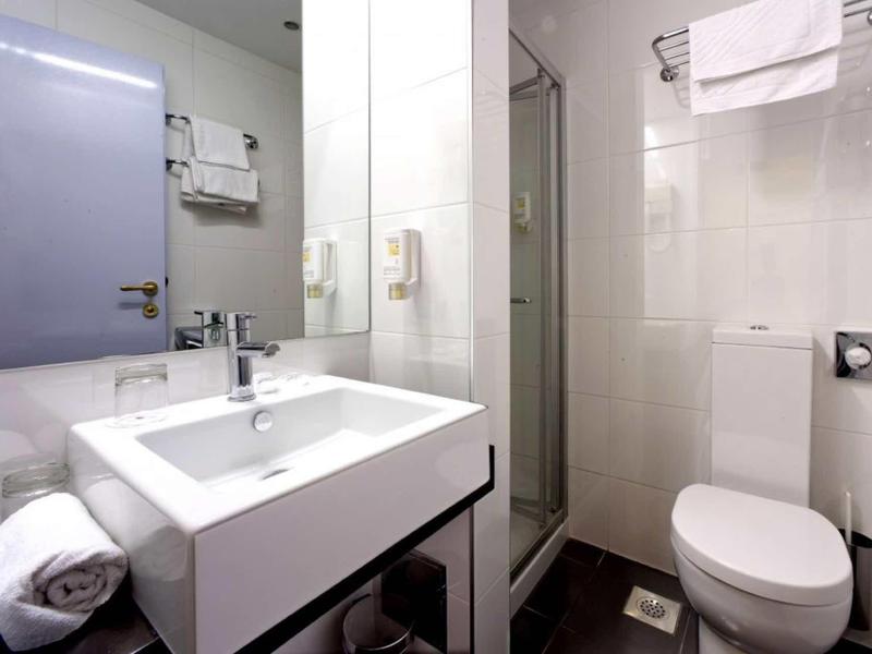 Kleines, modernes Badezimmer mit weißem Waschbecken, Spiegel, Dusche und Toilette.