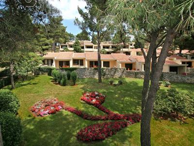 Gebouw met terrassen omgeven door een groene tuin met bomen en bloemstukken.