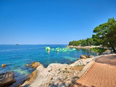 Een pad langs de rotsachtige kust met bomen en een opblaasbare speeltuin op de heldere blauwe zee.