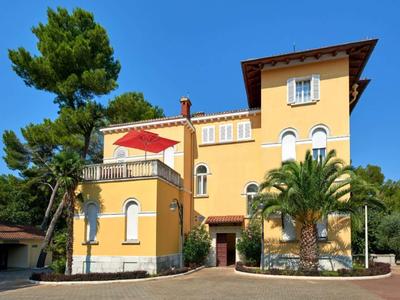 Geel hotelgebouw met rode parasol en palmbomen onder een blauwe lucht.