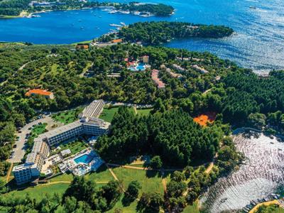 Vista aérea de un hotel con piscina, rodeado de bosque y costa junto al mar.