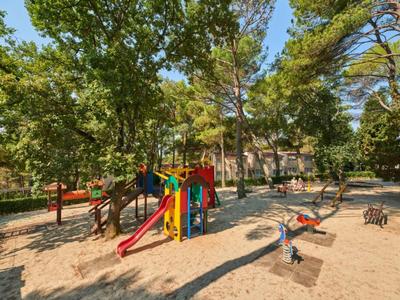 Parque infantil con tobogán colorido y balancín rodeado de árboles en un parque soleado.