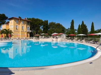 Groot rond hotelzwembad met parasols en gebouw op de achtergrond onder een heldere lucht.