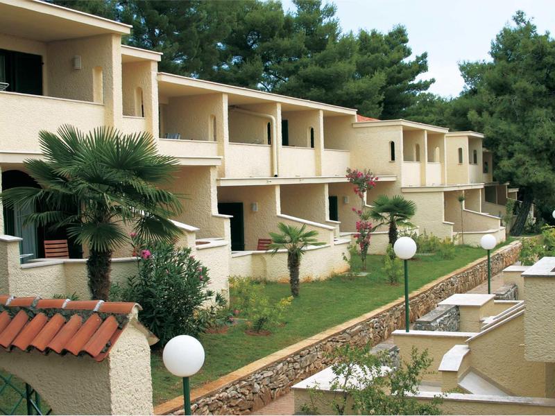 Complejo hotelero de varios pisos con balcones, palmeras y jardín cuidado al aire libre.