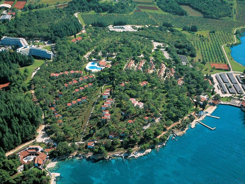 Complejo hotelero con numerosos edificios y piscinas junto a una costa boscosa y el mar.