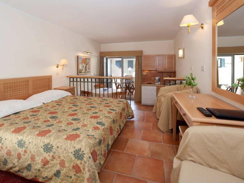 Habitación de hotel luminosa con cama doble, muebles de madera y acceso a un balcón con vista exterior.