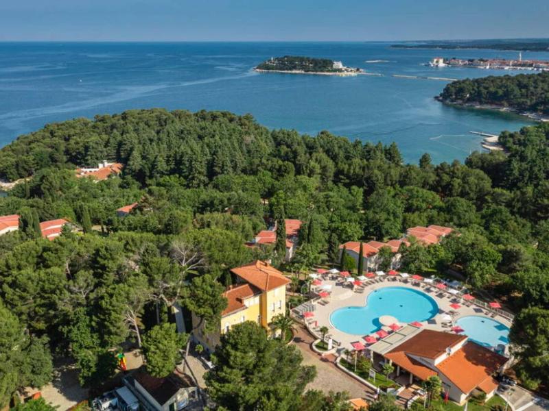 Vista de una piscina de hotel rodeada de árboles, con el mar y islas al fondo.