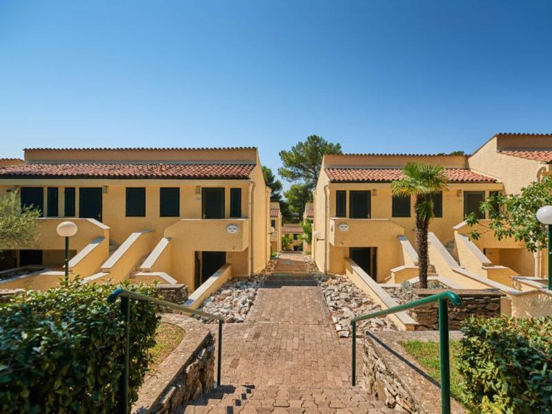 Complejo residencial con edificios amarillos, escaleras y camino de piedra bajo cielo azul en zona hotelera.