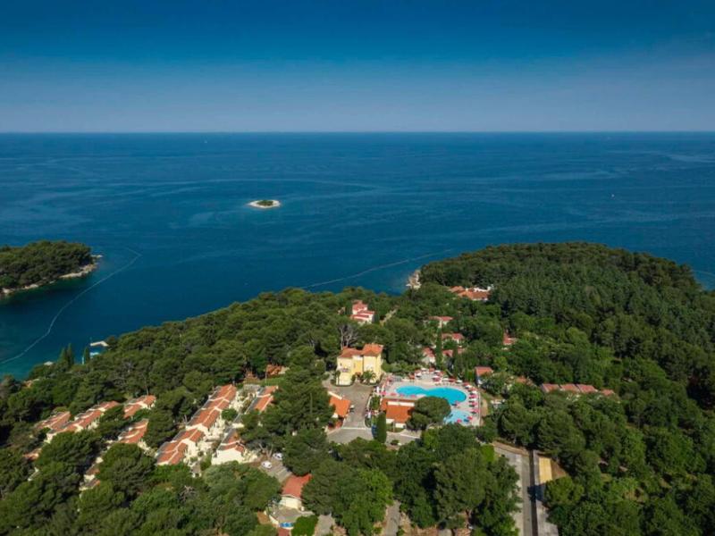 Toma aérea de un hotel con piscina en una zona costera boscosa junto al mar.