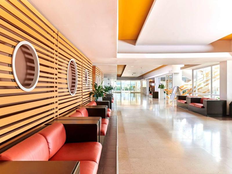 Moderna recepción de hotel con sillones rojos, revestimiento de madera y mucha luz natural.