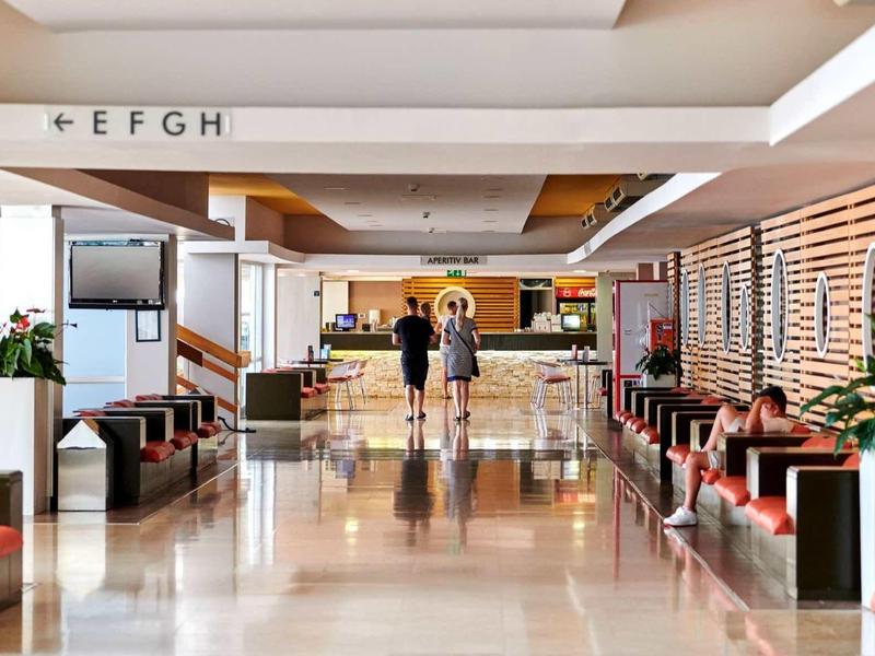 Amplia y luminosa zona de lobby de hotel con asientos e información en la recepción.