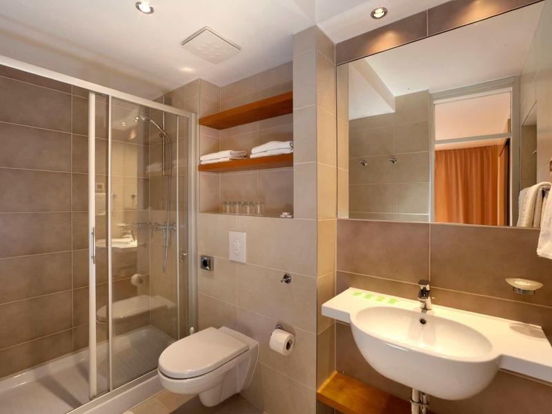 Baño moderno con cabina de ducha, inodoro de pared, lavabo y espejo grande.