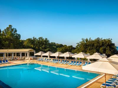 Großer Außenpool mit Liegestühlen und Sonnenschirmen unter blauem Himmel.