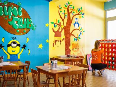 Sala giochi colorata per bambini con tavoli, sedie, giochi e murales in un hotel