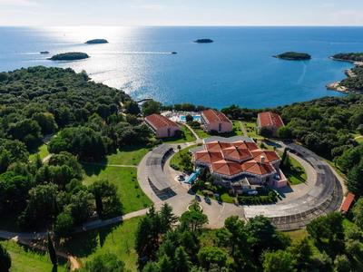 Hotel rotondo con tetti rossi circondato da foresta, vista sul mare blu e piccole isole.