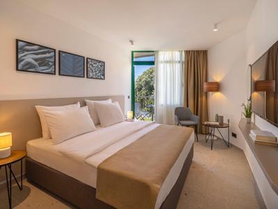 Accogliente camera d'hotel con letto matrimoniale, area salotto e balcone con vista sul giardino.