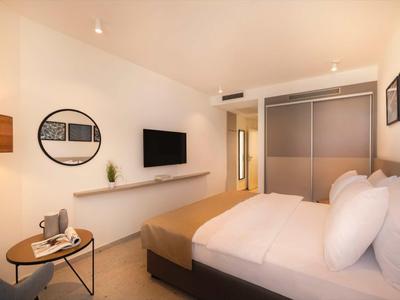 Camera d'hotel moderna con letto matrimoniale, TV a muro e piccolo tavolo rotondo con sedie.