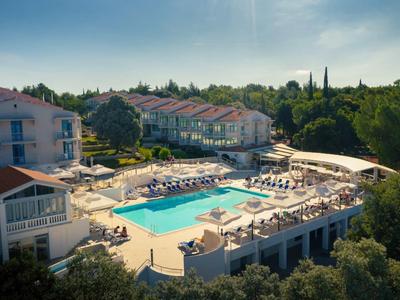 Hotel mit großem Pool auf der Terrasse, umgeben von Bäumen und Sonnenschirmen.