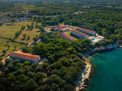 Complesso alberghiero con più edifici lungo la costa, circondato dalla foresta e affacciato sul mare.