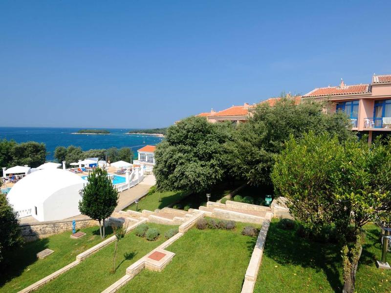 Complesso alberghiero con giardino, piscina e vista sul mare sotto cielo sereno.
