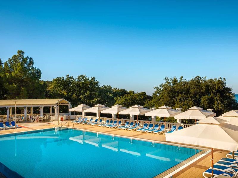 Grande piscina all'aperto con lettini e ombrelloni sotto un cielo azzurro.