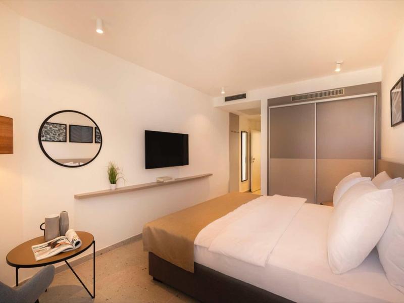 Camera d'hotel moderna con letto matrimoniale, TV a muro e piccolo tavolo rotondo con sedie.