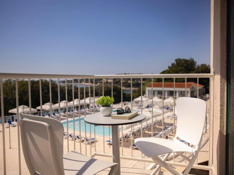 Piccolo balcone con sedie bianche e tavolo con vista su piscina e mare