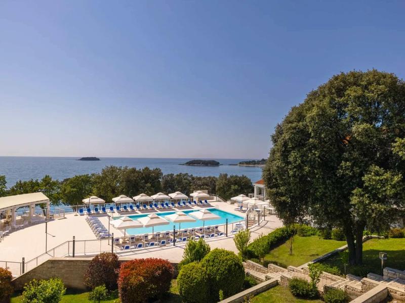 Vista panoramica di una piscina all'aperto con lettini e vista sul mare in una giornata di sole.
