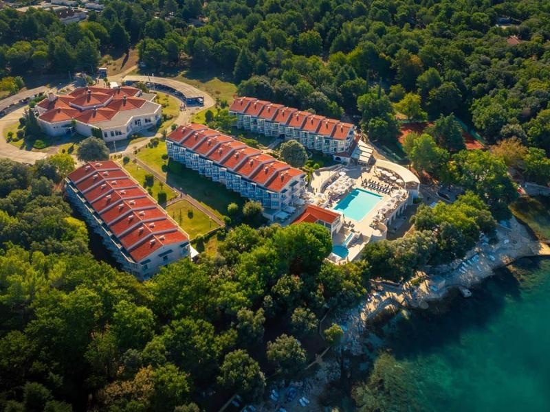 Complesso alberghiero con tetti rossi e piscina, circondato da foresta fitta vicino alla costa.