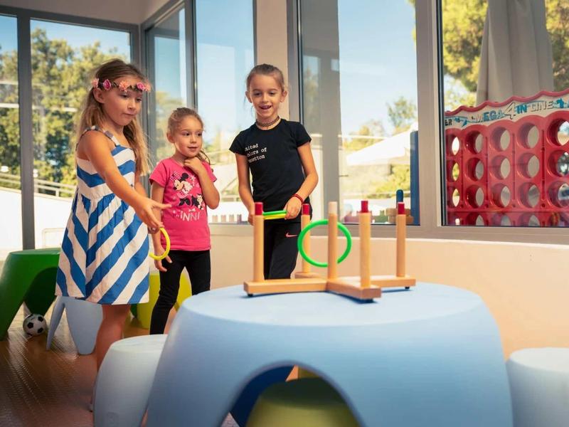 Tre bambini giocano con un giocattolo in un'area interna luminosa di un hotel.
