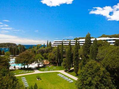 Zielony krajobraz parku hotelowego z basenem i leżakami pod niebieskim niebem.