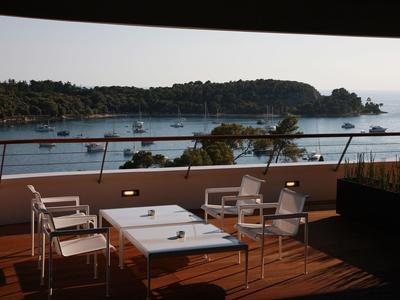 Taras z stołami i krzesłami z widokiem na morze i zalesiony półwysep.