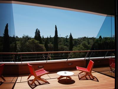 Balcon avec chaises rouges et petite table ronde devant des arbres verts sous un ciel clair