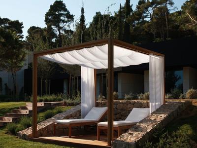 Drewniany pawilon z białymi zasłonami nad dwoma leżakami w ogrodzie.