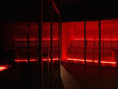 Ciemne pomieszczenie z czerwonym oświetleniem LED i szklanymi ścianami, prawdopodobnie nowoczesna strefa spa.