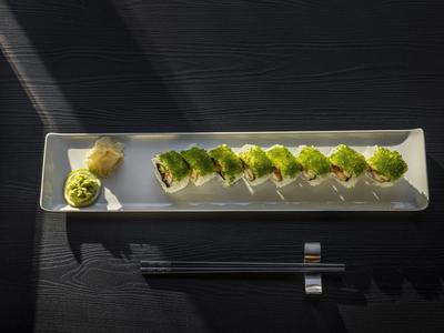 Długi biały talerz z rzędem sushi i wasabi, na ciemnym stole z pałeczkami.