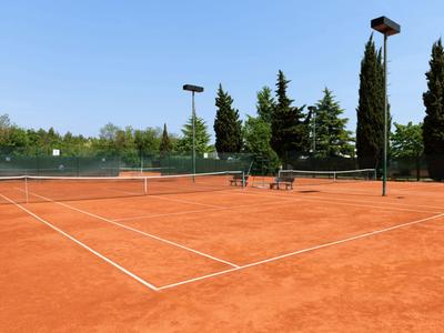 Terrain de tennis en terre battue rouge en plein air avec des arbres et une clôture bleue.