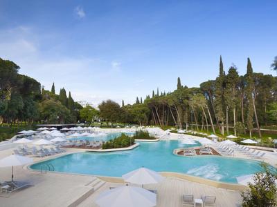 Espace piscine de loisirs avec plusieurs bassins, chaises longues et végétation environnante sous un ciel bleu