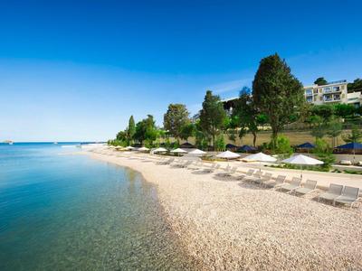 Breiter Sandstrand mit Liegen und Schirmen, klar blaues Wasser und Häuser auf grünen Hügeln.