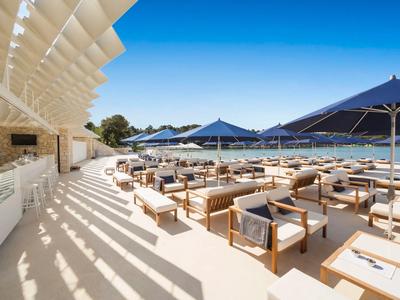 Espace extérieur moderne d'un hôtel avec fauteuils, parasols et vue sur la mer sous un ciel bleu.