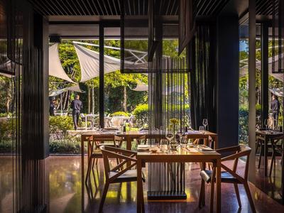 Przytulna restauracja z drewnianymi stołami i krzesłami, widok na zielony teren na zewnątrz.