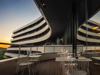 Terrasse d'hôtel moderne avec tables et chaises au coucher du soleil et façade en verre réfléchissant.