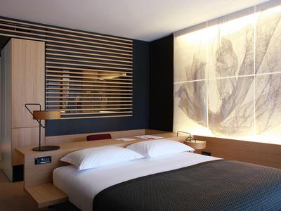 Modernes Hotelzimmer mit Holzdetails, großem Bett und stimmungsvoller Beleuchtung an der Wand.