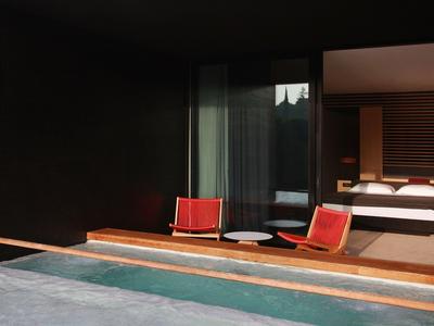 Moderner Hotelbalkon mit zwei roten Stühlen und Blick auf ein Schlafzimmer und einen Pool.