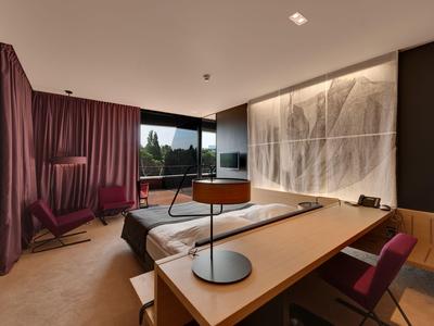Modernes Hotelzimmer mit großem Fenster, Schreibtisch, Fernseher und gemütlicher Sitzgelegenheit.