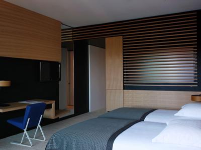 Modernes Hotelzimmer mit zwei Betten, blauem Stuhl, Holzverkleidung und sanfter Beleuchtung.