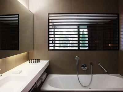 Modernes Badezimmer mit Badewanne, Waschbecken und großem Fenster mit Lamellen.